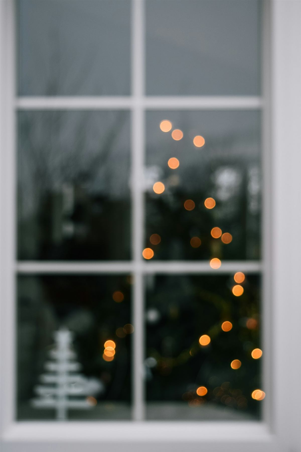 Fenster mit Schneeflocken, dahinter ein leuchtender Weihnachtsbaum